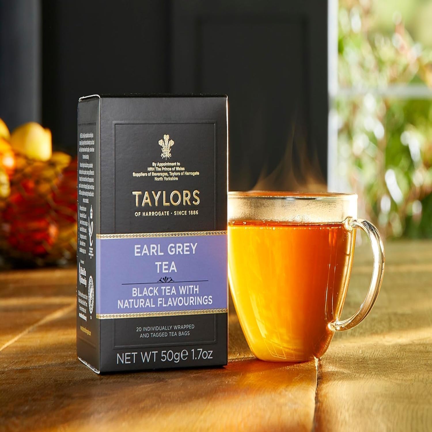 Taylors of Harrogate Earl Grey tea box with a steaming cup of tea on a wooden surface.